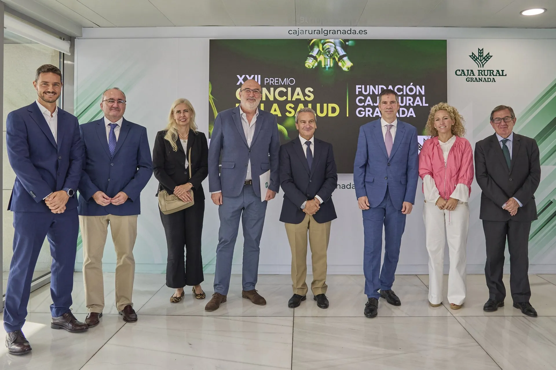 Ocho personas posan de pie ante una pantalla con el texto «XXII Premio Ciencias de la Salud Fundación Caja Rural Granada»; David Sancho, con traje azul y corbata rosa, es el sexto por la izquierda