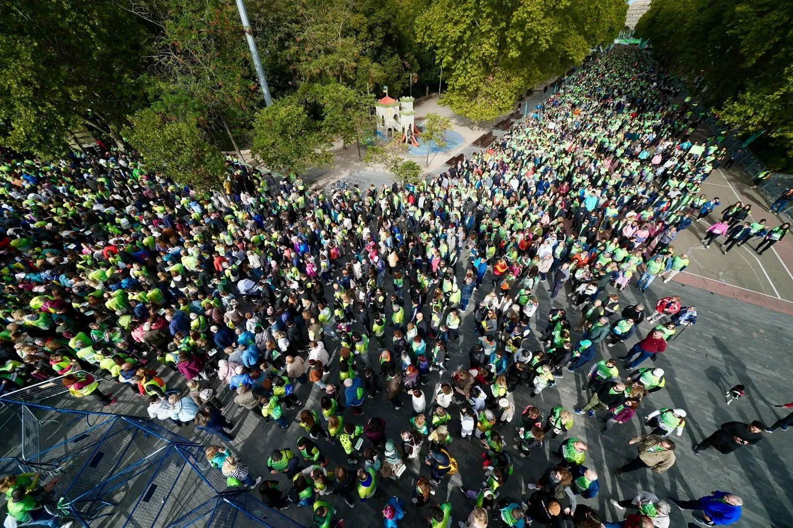 Vista desde lo alto de miles de participantes con camisetas verdes que ocupan toda una avenida junto a un parque infantil