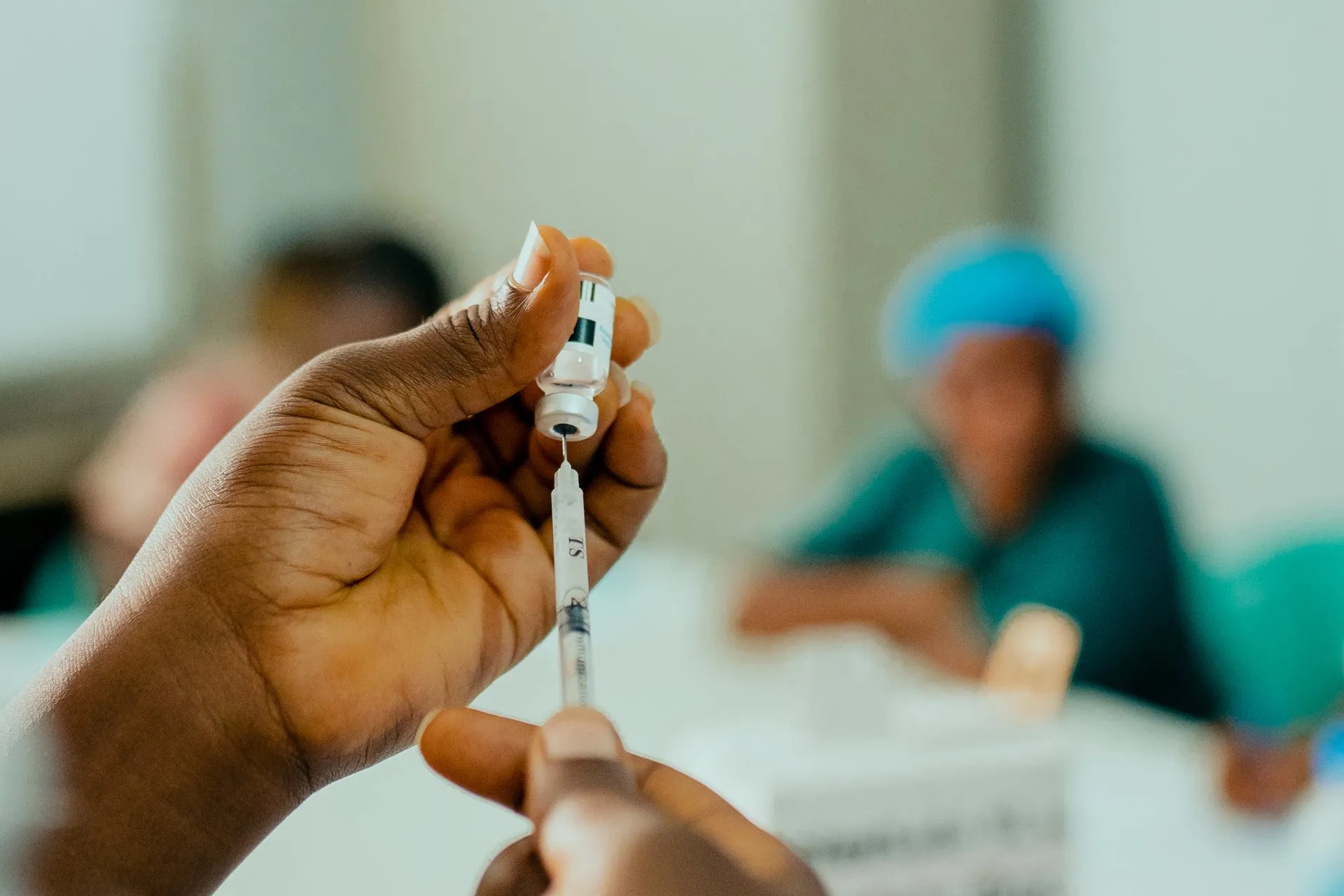 Una sanitaria carga una jeringa con la vacuna contra la mpox desde un vial, con otra trabajadora sanitaria desenfocada al fondo