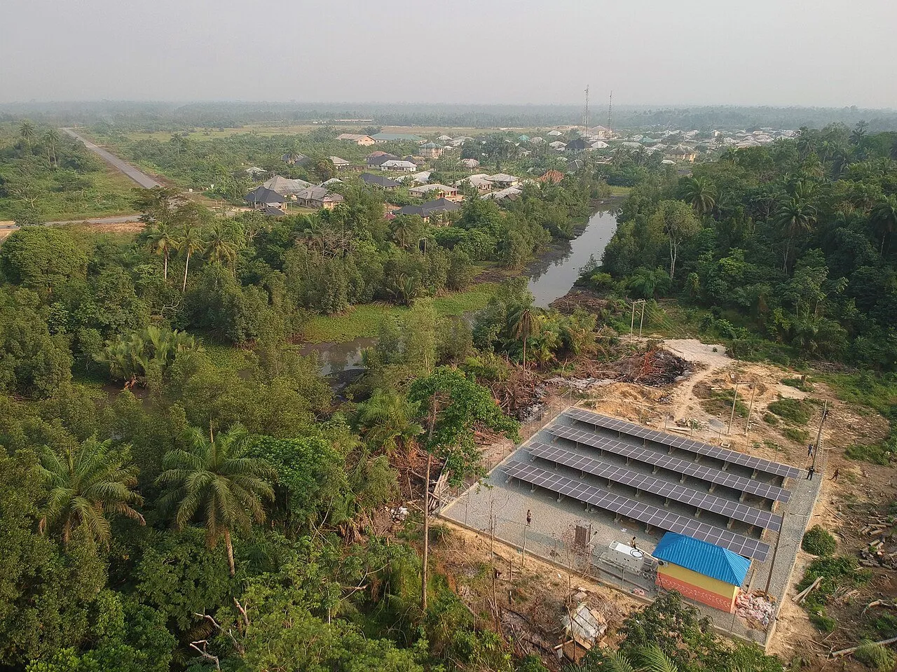 Vista aérea de una planta de placas solares junto a un pueblo rodeado de palmeras y selva