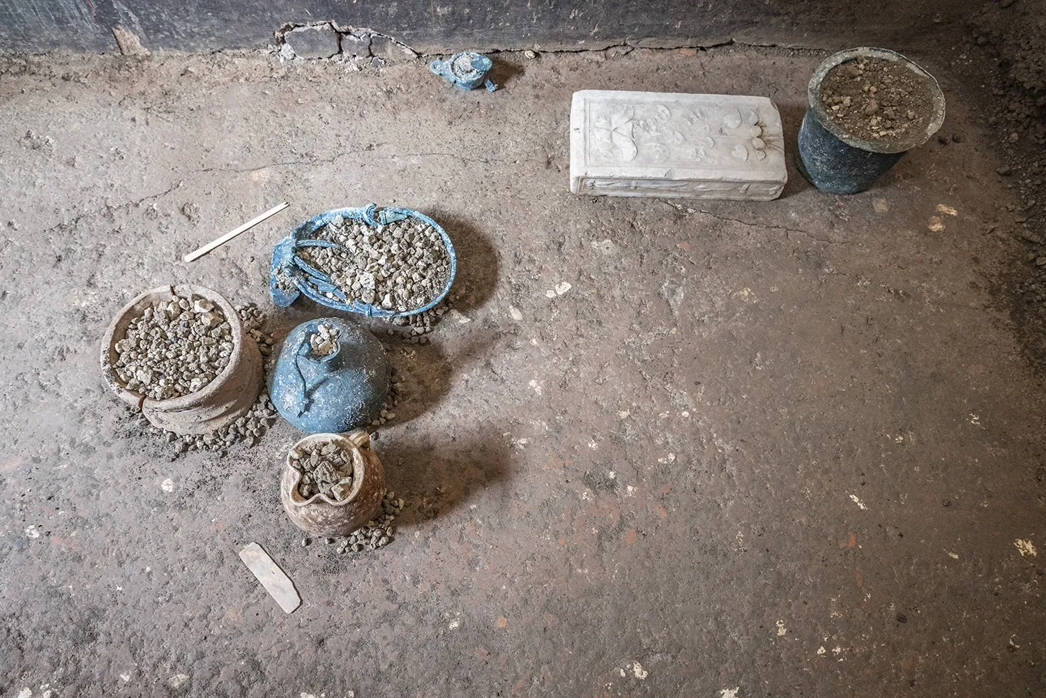 Vasijas de bronce y de cerámica cubiertas de tierra junto a una caja de mármol blanco, en el suelo de una excavación